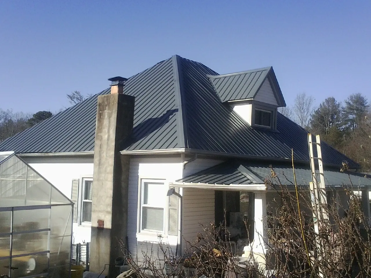 Dark blue standing seam metal roof on a white farmhouse with dormer — Slate & Tile Roof Repair by Roofing Brothers in Pilot Point