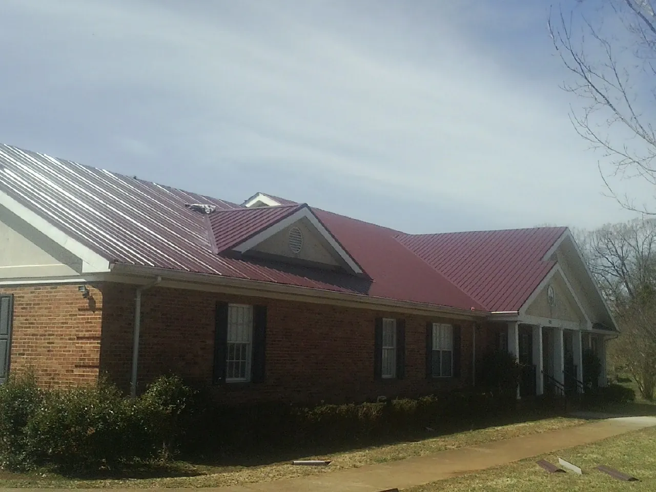 Red metal roof with gabled entries on a long brick building, from a Hail Damage Roof Repair job in Pilot Point