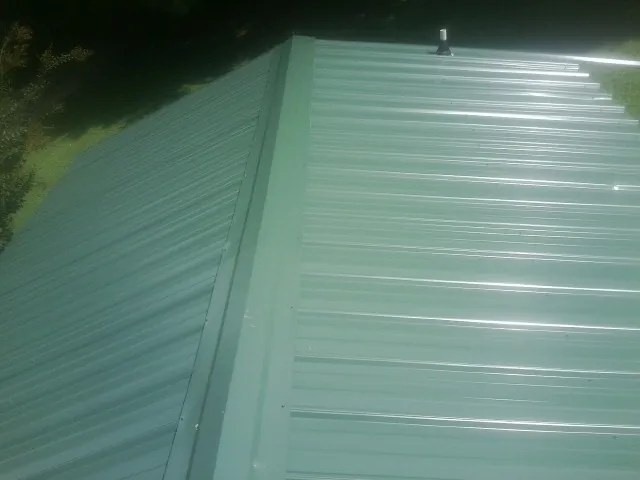 New green metal panels meeting at the ridge of a roof — Flat Roof Repair work by our crew in Pilot Point