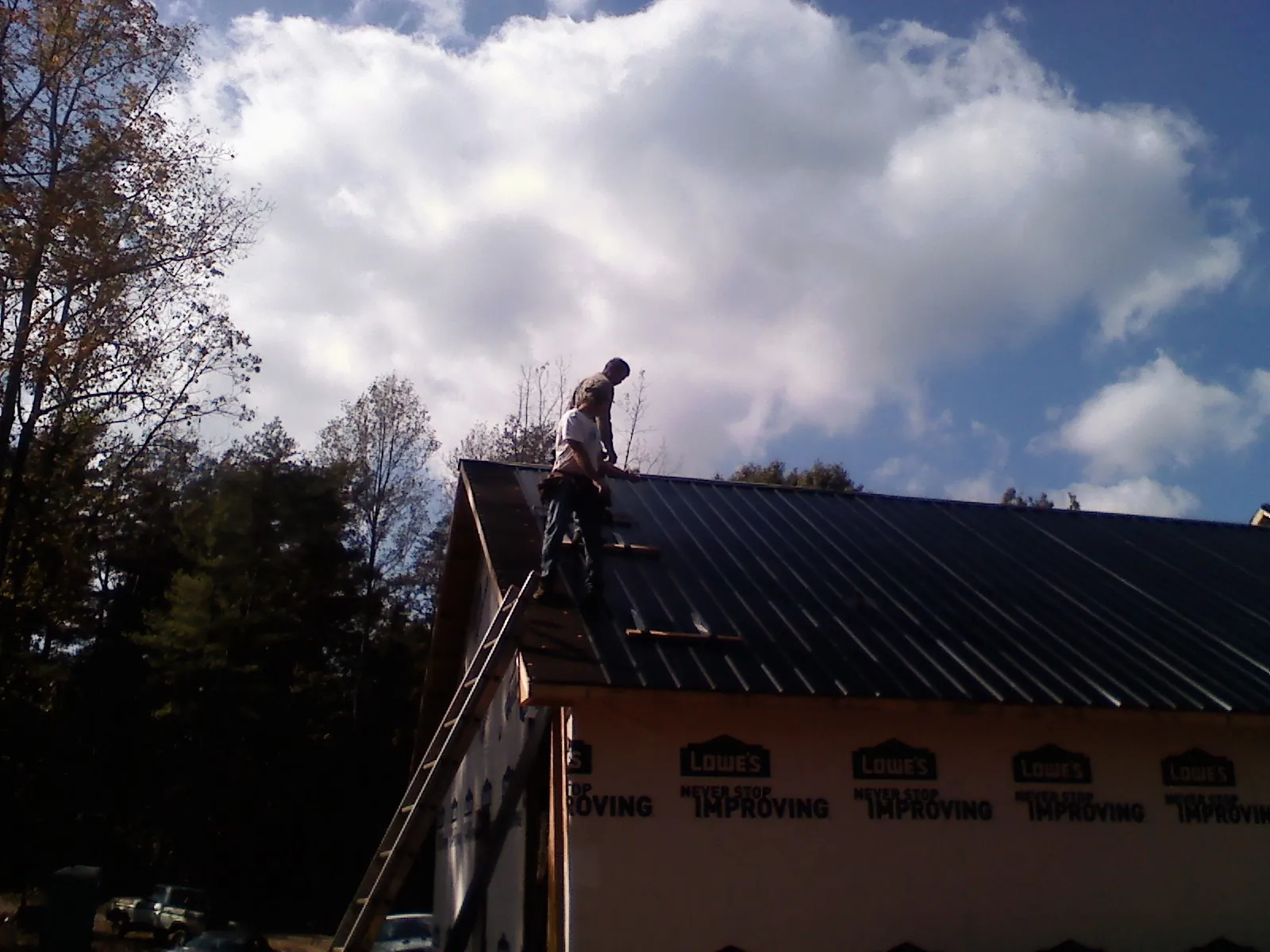 Roofer fastening dark metal panels high against a cloudy sky, from a Roof Inspection job in Pilot Point