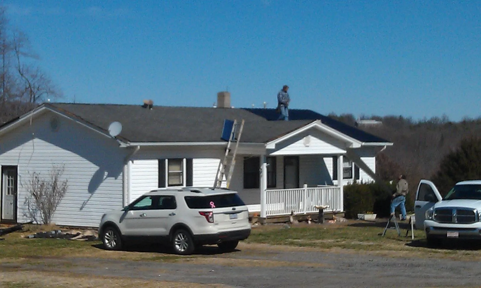 Roofers stripping shingles from a white ranch house roof in Pilot Point