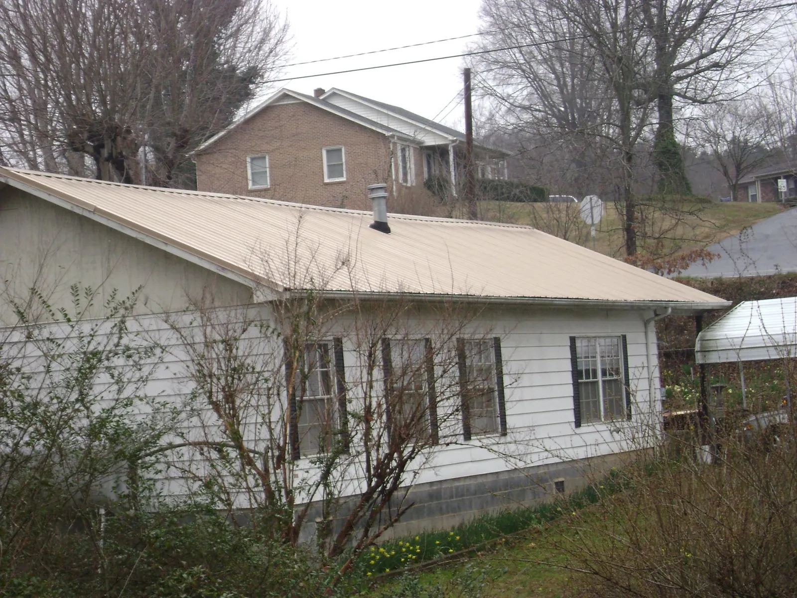 Tan metal roof on a white sided house set into a hillside — Commercial Roofing by Roofing Brothers in Pilot Point