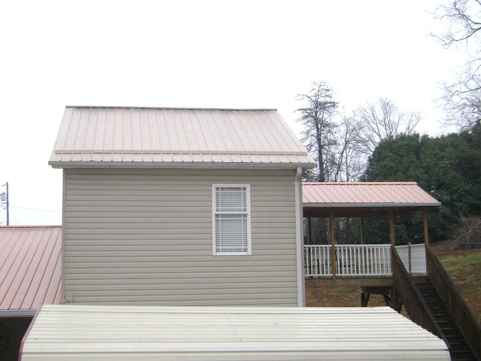 Tan metal roofs on a two story addition and attached porch, from a Roof Replacement job in Pilot Point